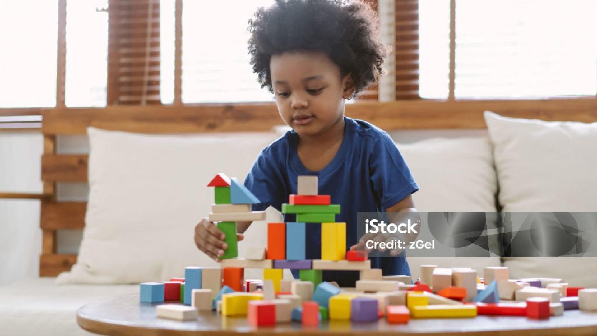 Little African american boy building a small house with colorful wooden blocks in living room at home. Educational toys for preschool and kindergarten children.